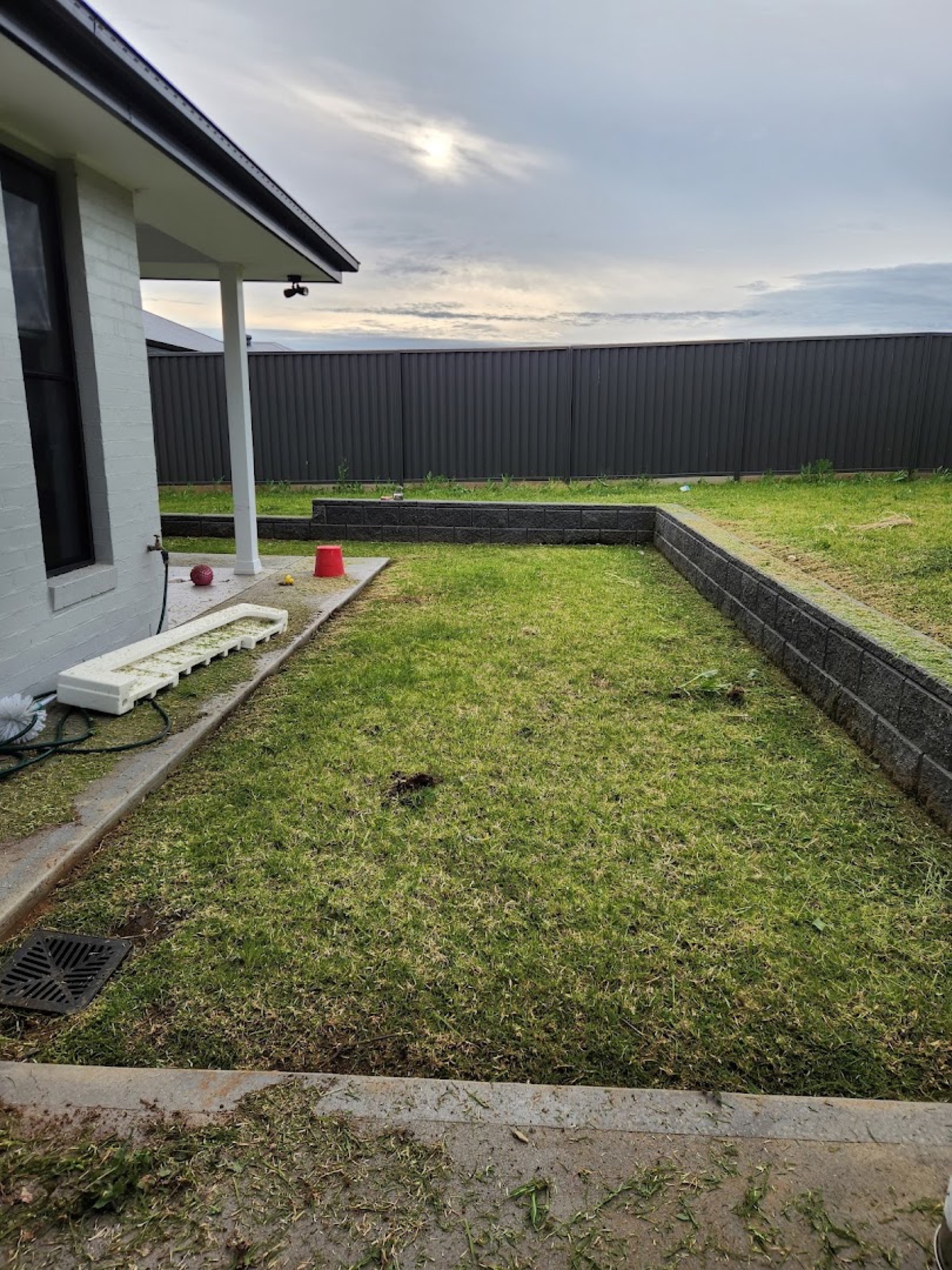 A mown back lawn running to a retaining wall under a heavy Dubbo sky