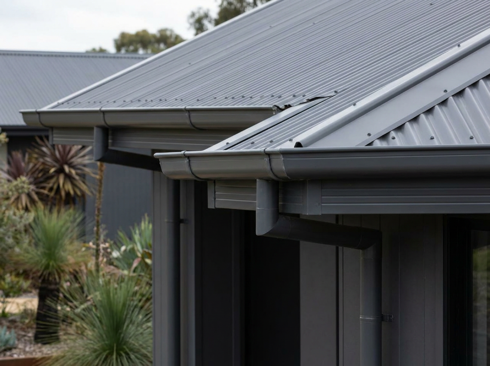 Gutters and downpipes running along the edge of a metal roof on a single storey home