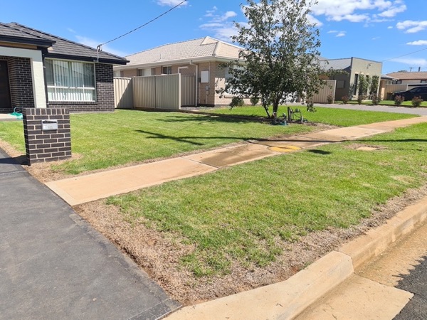 A mown front lawn and nature strip beside a concrete footpath