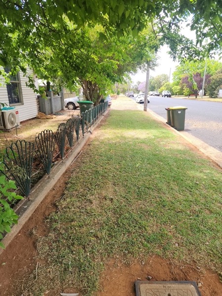A nature strip mown along a street beside a footpath and wheelie bins