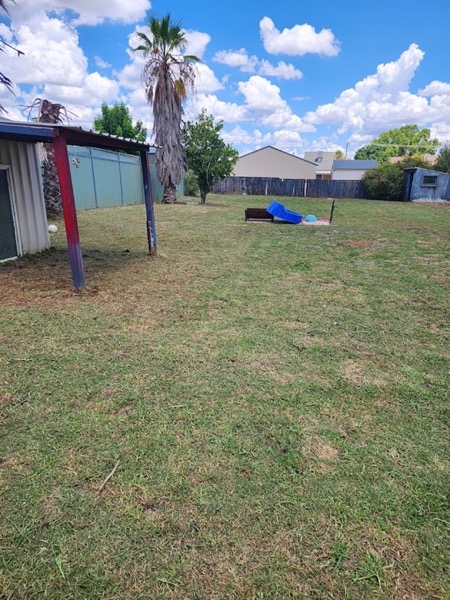 A large back yard mown flat beside a shed and a carport
